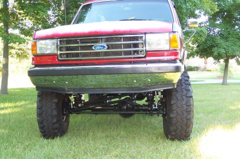 1990 Ford Bronco - This lifted Ford Bronco features a chrome bumper and a prominent grille with the Ford logo.