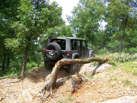 1992 Jeep YJ - Olive green Jeep Wrangler navigates a challenging off-road trail, maneuvering around a large fallen tree.