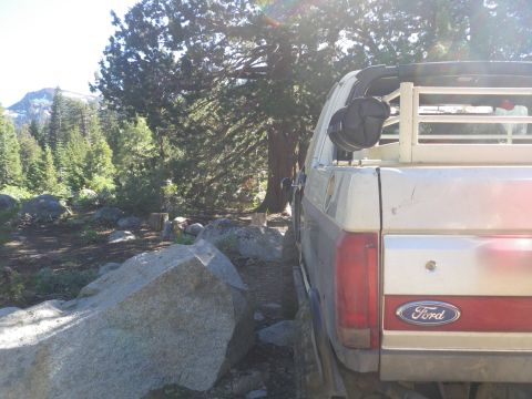 1991 Ford Bronco - The rear of a 1991 Ford Bronco is visible, parked off-road amidst trees and large rocks.