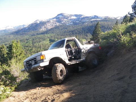 1991 Ford Bronco - A white 1992 Ford Bronco navigates a steep dirt trail amidst a mountainous, forested landscape.