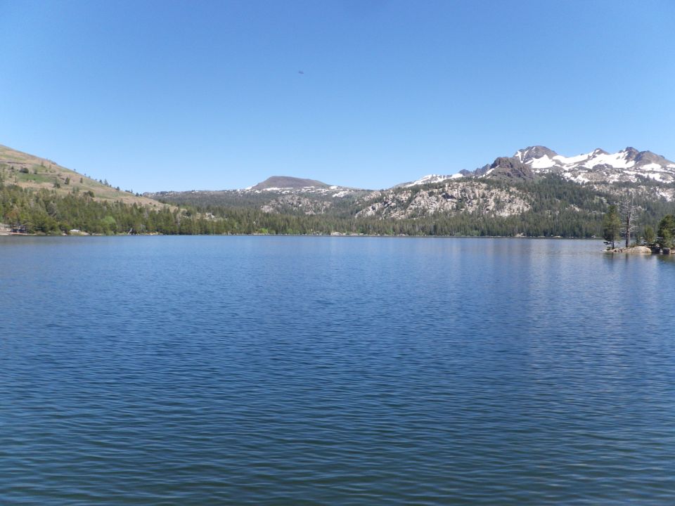 Lake with mountains and trees under a clear blue sky. "SUPERMOTORS www.supermotors.net" logo in lower right