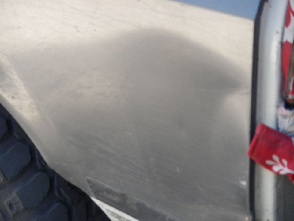 Silver vehicle side panel with tire and red fabric hanging from a trim piece