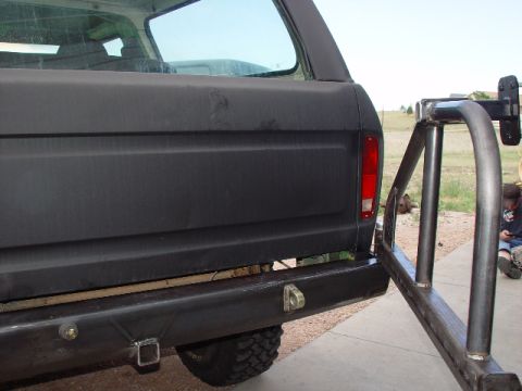 1978 Ford Bronco - The rear of a black Ford Bronco shows a custom bumper and a swing-away tire carrier, with a person visible in the background.