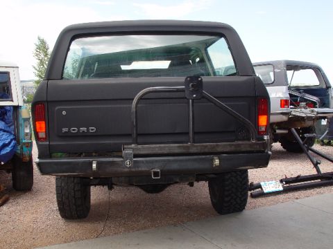 1978 Ford Bronco - The rear of a black Ford Bronco is shown with a custom bumper and spare tire carrier, parked next to another vehicle.
