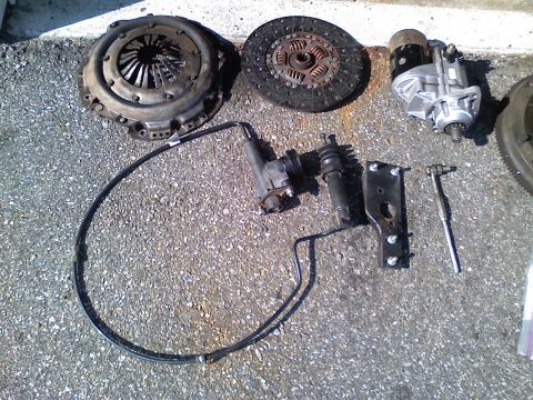 1990 Ford Bronco - Various automotive parts, including a clutch kit and starter, are arranged on a gravel surface.