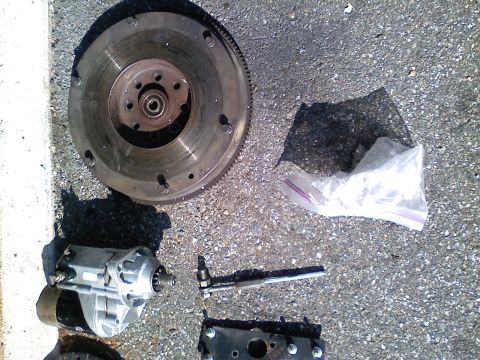 1990 Ford Bronco - Various automotive parts, including a flywheel and starter motor, are laid out on a paved surface.