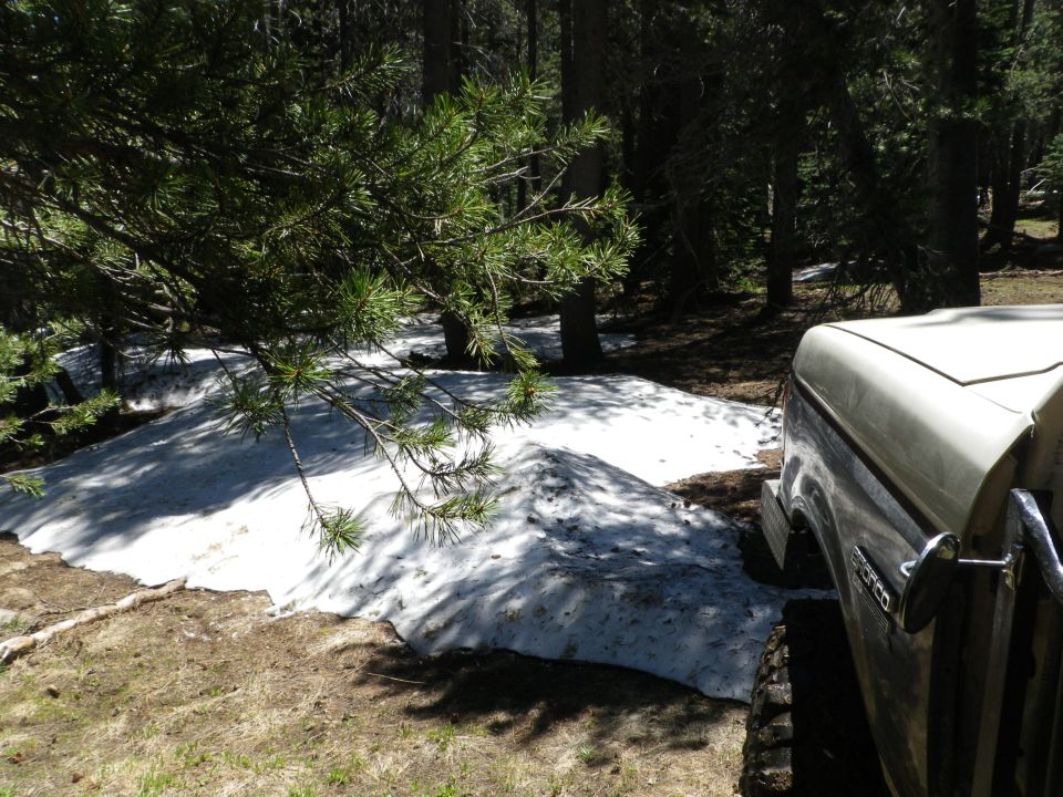 Cream-colored Ford Bronco parked on dirt with snow patches, seen from the front-right