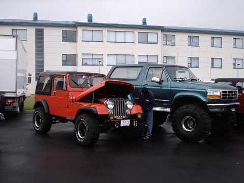1996 Ford Bronco - A green 1996 Ford Bronco is parked next to an orange Jeep, both modified with large tires.