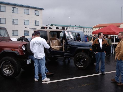 1996 Ford Bronco - Two Jeeps are parked side-by-side at an outdoor event with people milling around.