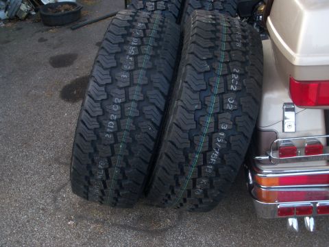 1989 Ford Bronco - Two off-road tires are positioned beside the rear of a motorcycle, which features chrome detailing and red taillights.