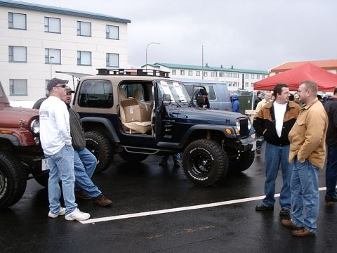 1996 Ford Bronco - A dark blue Jeep Wrangler with a tan top and roof rack is parked on a wet surface, with its doors open.