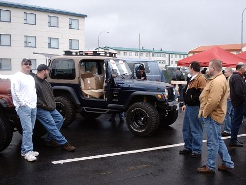 1996 Ford Bronco - A dark blue Jeep Wrangler is parked outdoors with its door open, alongside another Jeep and several onlookers.