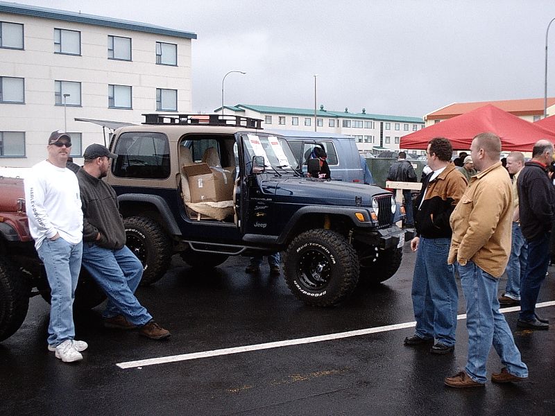 Dark blue Jeep Wrangler with big tires and roof rack at an outdoor car meet