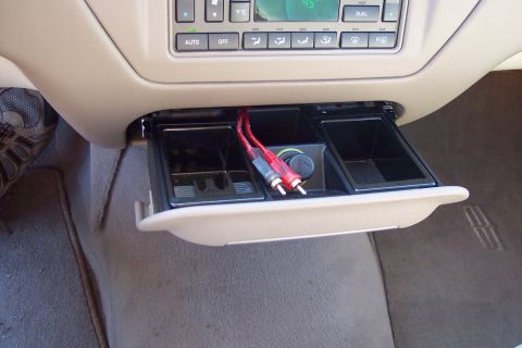 2001 Ford Crown Victoria - The interior of a beige vehicle shows an open compartment with audio cables and a 12v power outlet.
