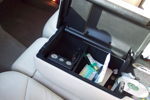 2001 Ford Crown Victoria - The interior of a car shows an open center console filled with various items including coins, keys, and a CD.