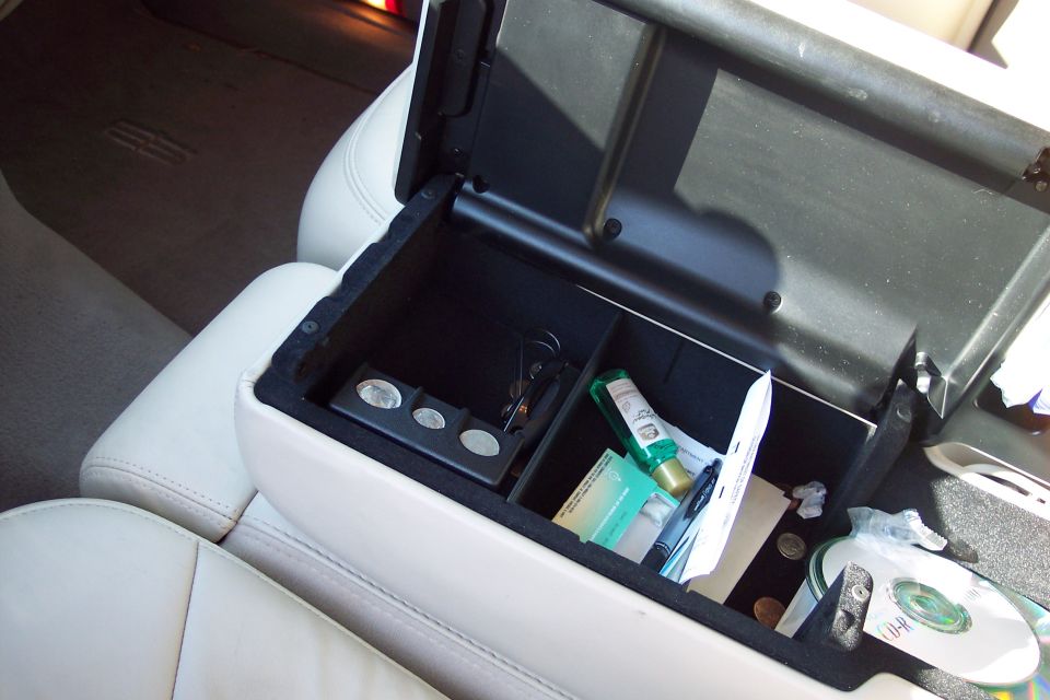 Car's open center console with coins, keys, a small bottle, and a CD