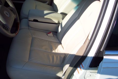 2001 Ford Crown Victoria - The interior of a car features light-colored leather seats and a center console with a red seatbelt buckle visible.