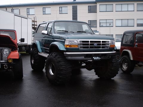 1996 Ford Bronco - A modified green Ford Bronco with large off-road tires sits parked next to other vehicles.