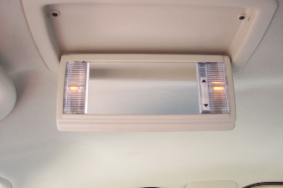 Interior overhead console with a mirror and two lights, one on each side. There are up and down arrows on the right light