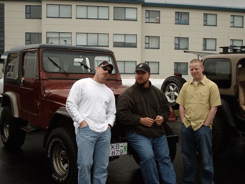 1996 Ford Bronco - Three men pose with a red Jeep Wrangler in front of a modern building.