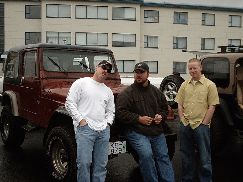 Three men posing beside a maroon Jeep Wrangler in a parking lot