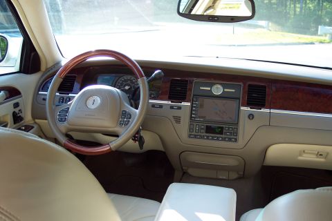 2001 Ford Crown Victoria - The interior of a Lincoln Town Car features a wood-trimmed steering wheel, a central navigation screen, and tan leather upholstery.