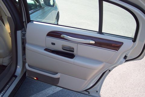 2001 Ford Crown Victoria - The interior door panel of a car features wood trim and a chrome grab handle, with another vehicle visible outside.