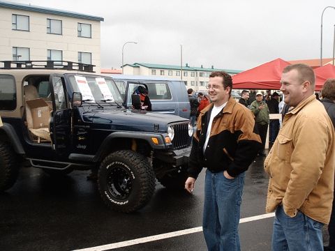 1996 Ford Bronco - Two men stand next to a Jeep Wrangler at an outdoor event, with a blue van in the background.