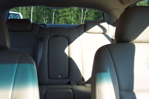 2001 Ford Crown Victoria - The interior rear seats of a car are visible, with light-colored leather upholstery and a view of trees through the back window.