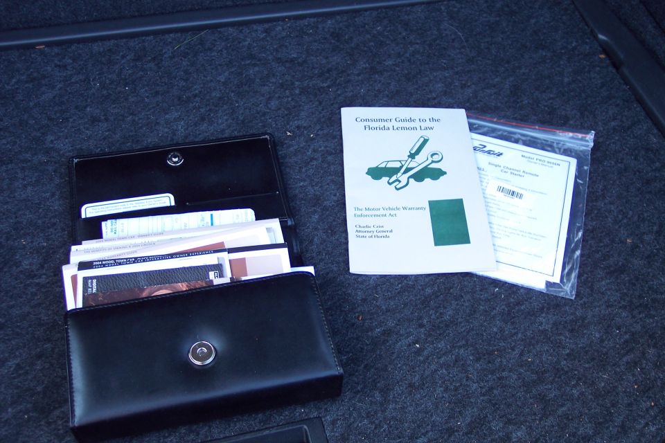 Car owner's manual and Florida Lemon Law guide in a black wallet, next to a plastic bag with more papers
