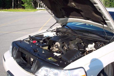 2001 Ford Crown Victoria - The engine bay of a white sedan is shown with the hood raised, revealing the engine and various components.