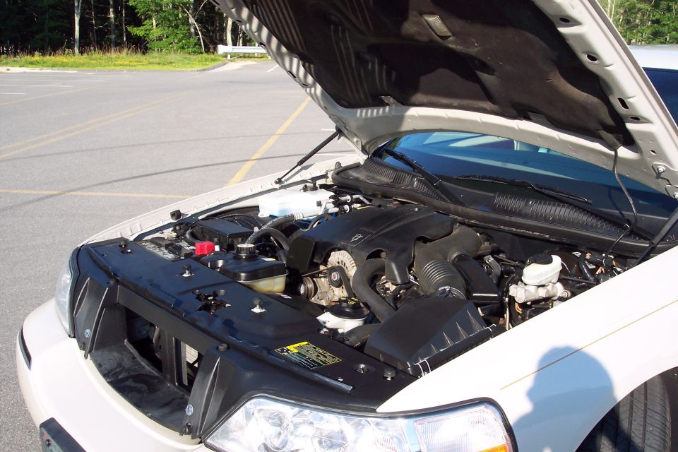 White car engine bay with hood open. Visible components include the engine, battery, and fluid reservoirs