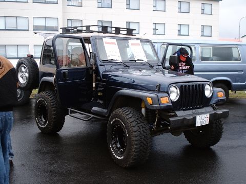 1996 Ford Bronco - A dark blue Jeep Wrangler is parked on a wet surface next to a blue van.