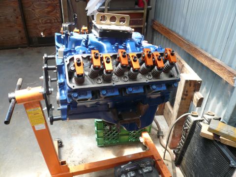 1975 Ford Ranchero - A blue engine with orange valve covers is mounted on an orange engine stand, ready for installation or work.