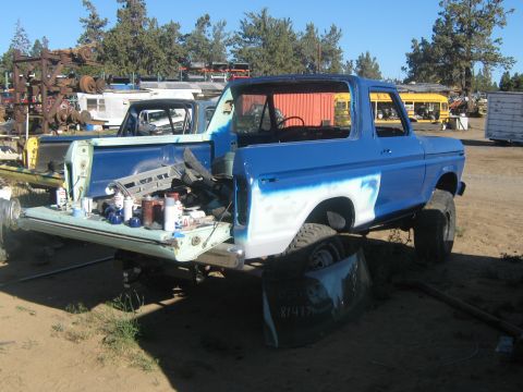 1978 Ford Bronco - A blue 1978 Ford Bronco is seen in a junkyard, with its tailgate open and parts laid out, suggesting it is undergoing repairs or restoratio…