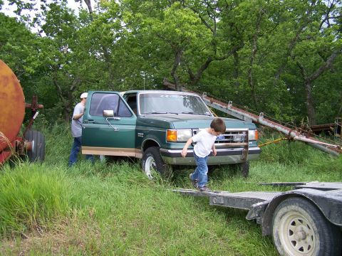1989 Ford Bronco - A green Ford F-Series truck is parked in a grassy area with a boy walking on a trailer in front of it.