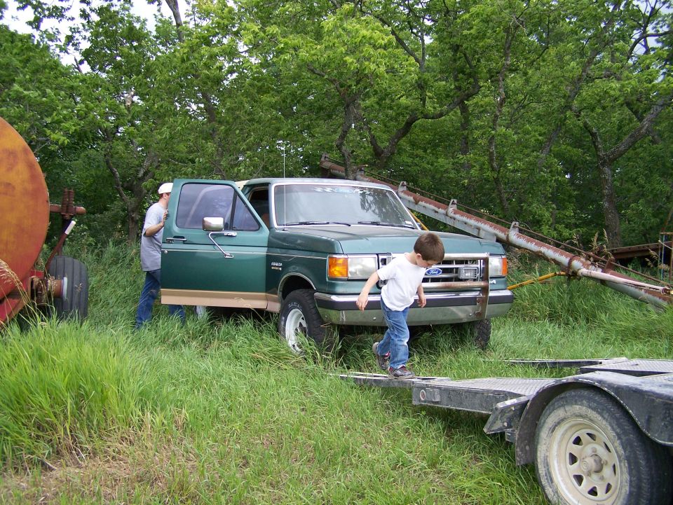 Green 1987 Ford F-Series truck, 3q-front view, with a boy on a trailer