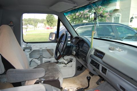 1994 Ford Bronco - The interior of a Ford truck shows the dashboard, steering wheel, and seats. The door panel is missing.