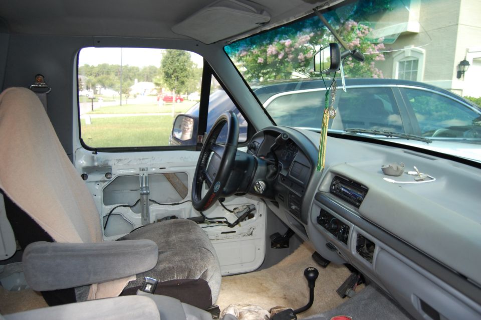 Interior of a Ford truck, showing the dashboard, steering wheel, and seats. The door panel is removed