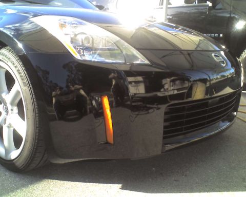 1993 Ford C-350 (Centurion Conversions) - Front view of a black Nissan 350Z, showing the bumper, grille, and headlight, with another vehicle reflected.