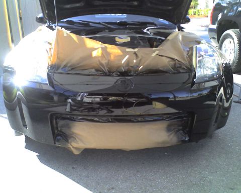 1993 Ford C-350 (Centurion Conversions) - Front end of a black car is covered in masking paper and tape, with the hood open, suggesting it is being prepped for painting.