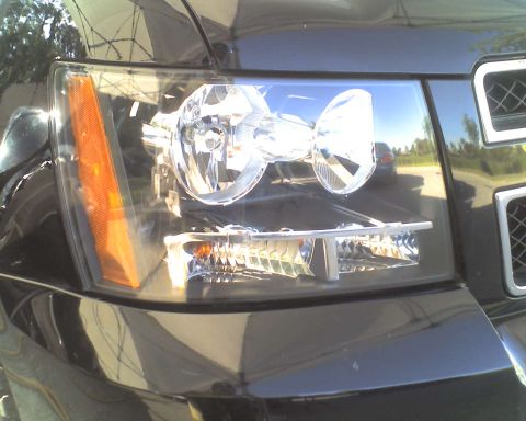 1993 Ford C-350 (Centurion Conversions) - The headlight assembly and part of the grille of a dark-colored vehicle are shown in this close-up shot.