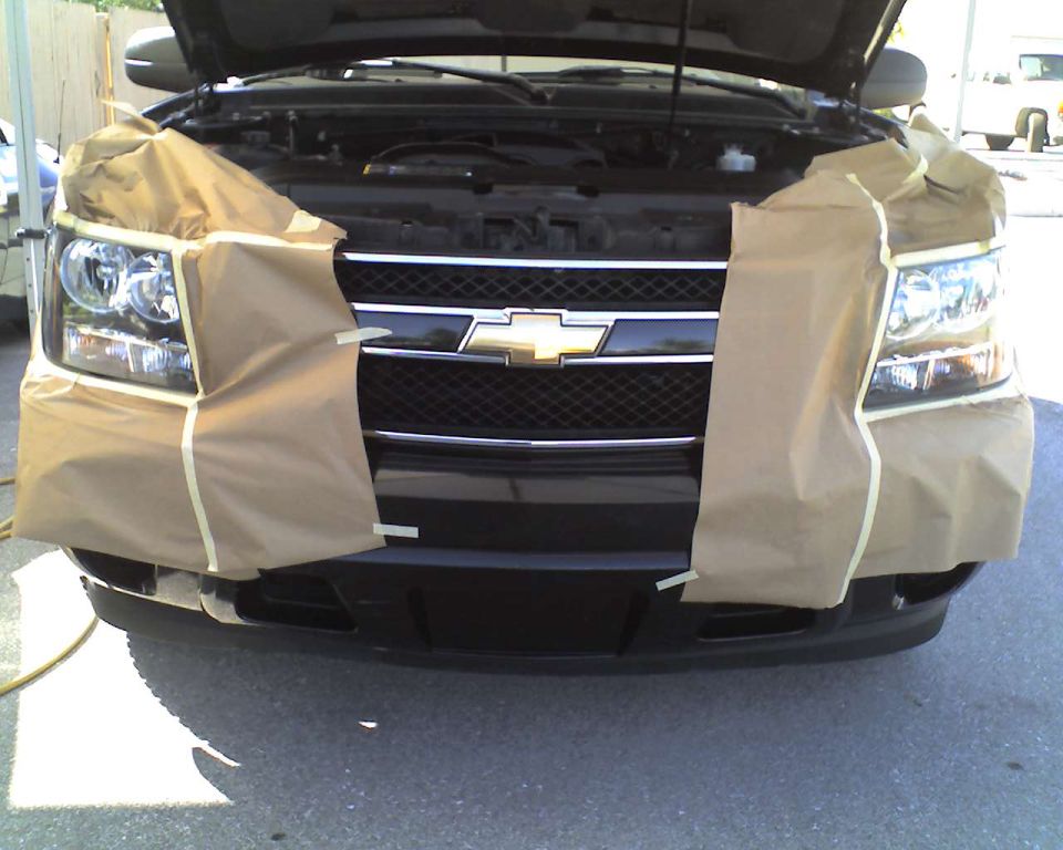 Black Chevrolet SUV front end masked with paper and tape for paint work, hood up