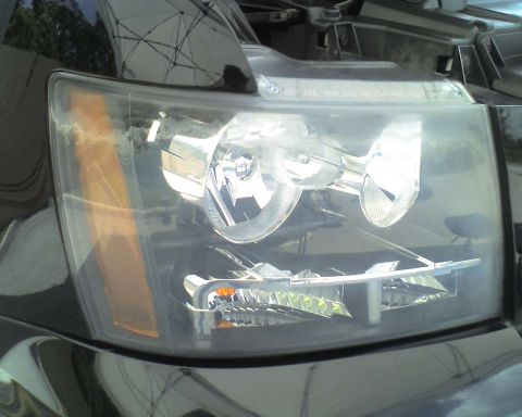 1993 Ford C-350 (Centurion Conversions) - The headlight assembly of a black vehicle is shown in detail, with the turn signal light on the left.