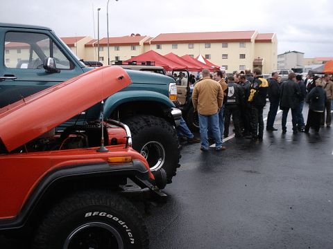 1996 Ford Bronco - A red Jeep with its hood up is parked next to a large green truck, with a crowd gathered in the background.