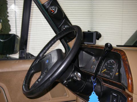 1990 Ford Bronco - Driver's-side dash view of a square-body truck with tan interior, black leather-wrapped steering wheel, wood-grain instrument bezel and an…
