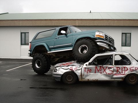 1996 Ford Bronco - A lifted 1992 Ford Bronco is parked on top of a heavily damaged car. The car has red writing on its side.