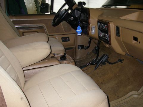 1990 Ford Bronco - Tan interior of a pickup truck showing front bench seat, dash, steering wheel, aftermarket radio, CB handset and a hanging air freshener.