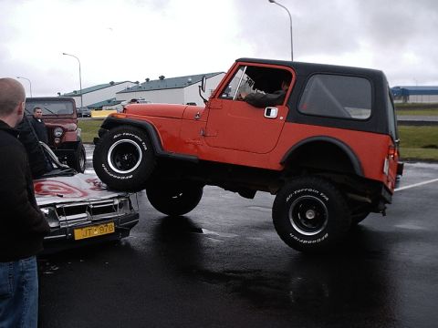 1996 Ford Bronco - A red Jeep CJ-7 is shown driving over a damaged car, with another Jeep visible in the background.