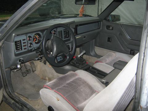 1985 Ford Mustang - The interior of a 1985 Ford Mustang is visible, a dashboard with gauges, a steering wheel, and cloth seats.